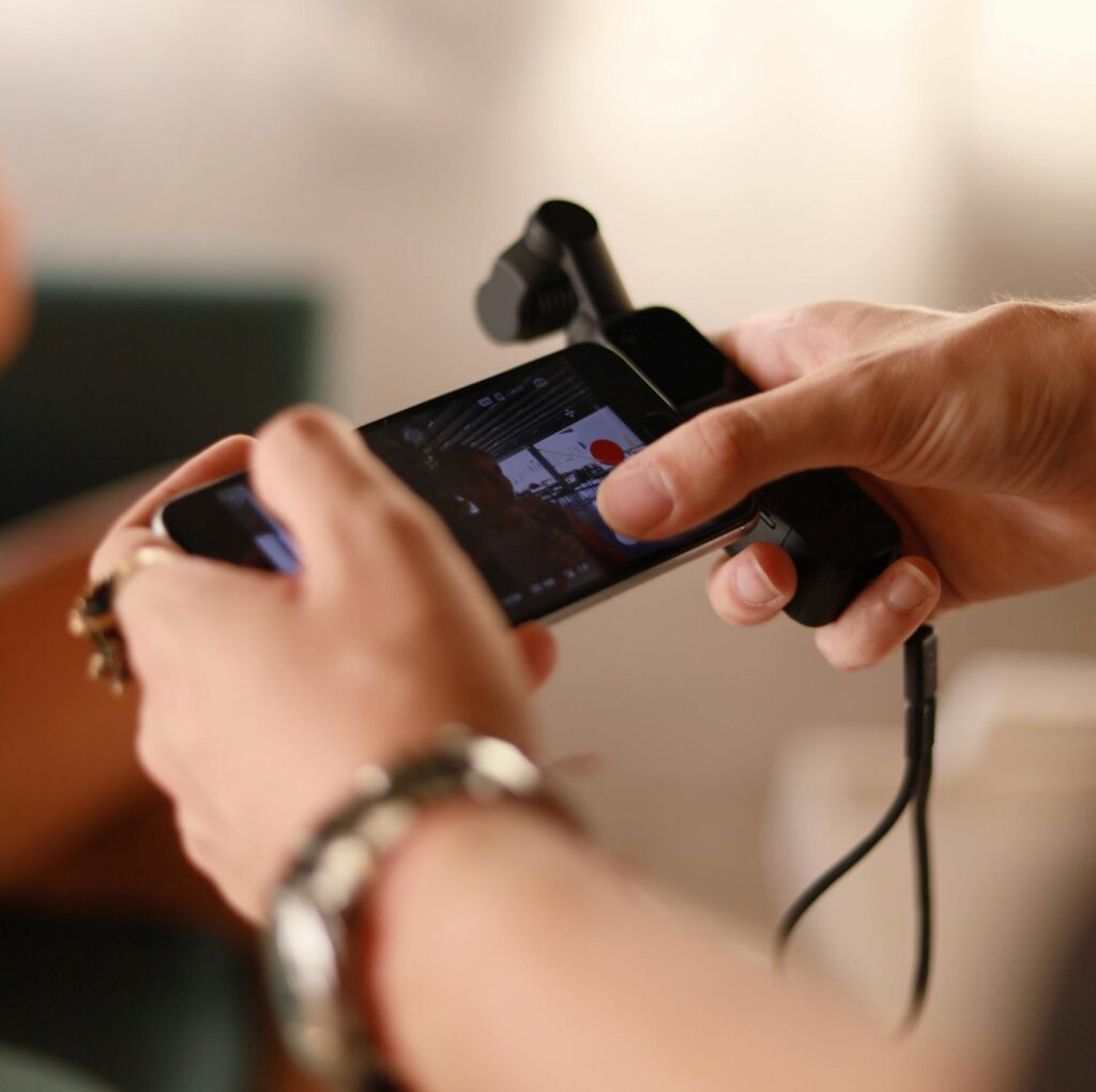 Hands using a smartphone with a microphone attachment for recording indoors.